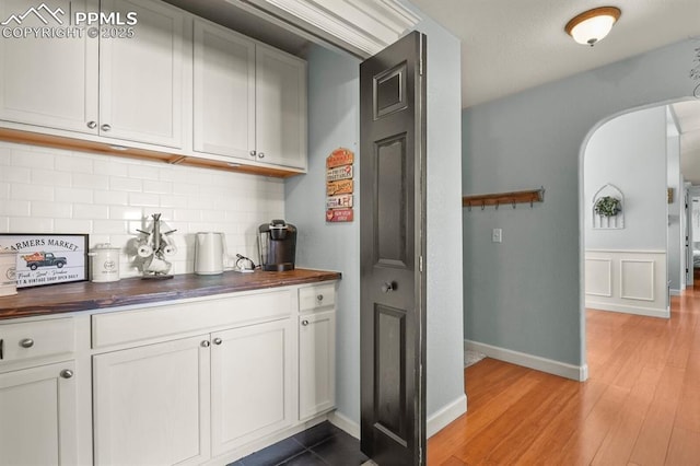 bar featuring baseboards, arched walkways, backsplash, and light wood-type flooring