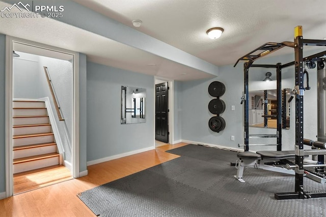 exercise area with a textured ceiling, baseboards, and wood finished floors