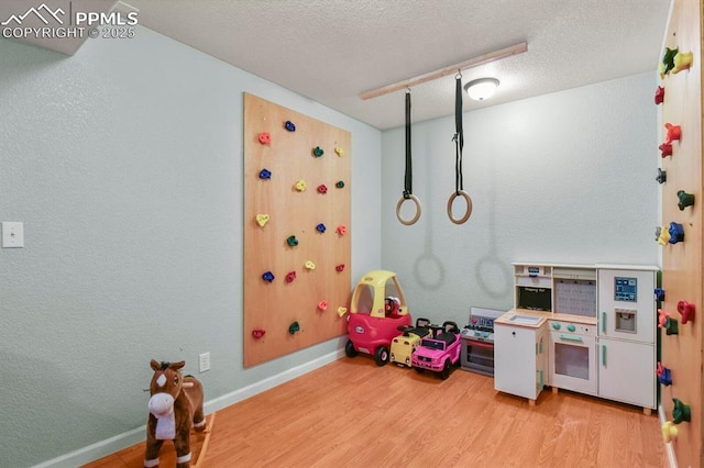 game room featuring wood finished floors, baseboards, a textured wall, and a textured ceiling