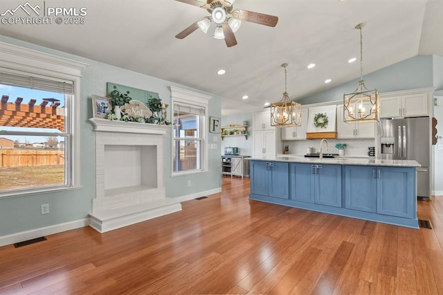 kitchen with light wood finished floors, a brick fireplace, stainless steel fridge with ice dispenser, white cabinetry, and a sink