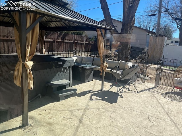 view of patio with a gazebo, a hot tub, an outdoor living space with a fire pit, and fence