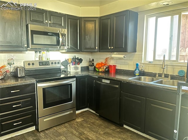 kitchen featuring dark countertops, dark wood finished floors, decorative backsplash, appliances with stainless steel finishes, and a sink