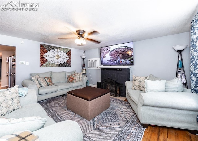 living room with a fireplace, wood finished floors, a textured ceiling, a wall mounted AC, and a ceiling fan