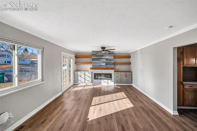 unfurnished living room with a ceiling fan, dark wood-style floors, baseboards, ornamental molding, and a large fireplace