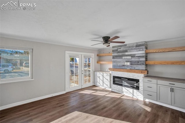 unfurnished living room with dark wood-type flooring, french doors, a stone fireplace, baseboards, and ceiling fan