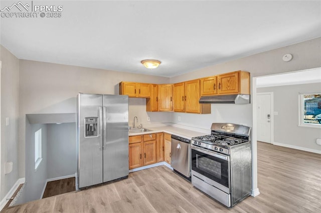 kitchen with light wood finished floors, a sink, light countertops, under cabinet range hood, and appliances with stainless steel finishes