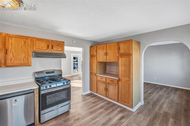 kitchen with wood finished floors, arched walkways, under cabinet range hood, and stainless steel appliances