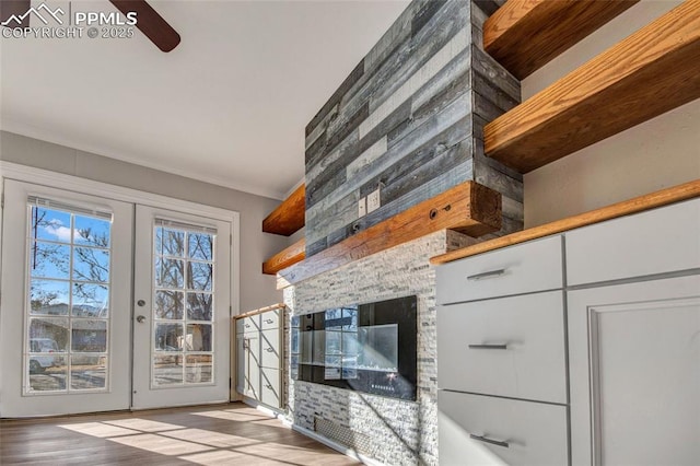 living area with wood finished floors, french doors, a multi sided fireplace, and ornamental molding