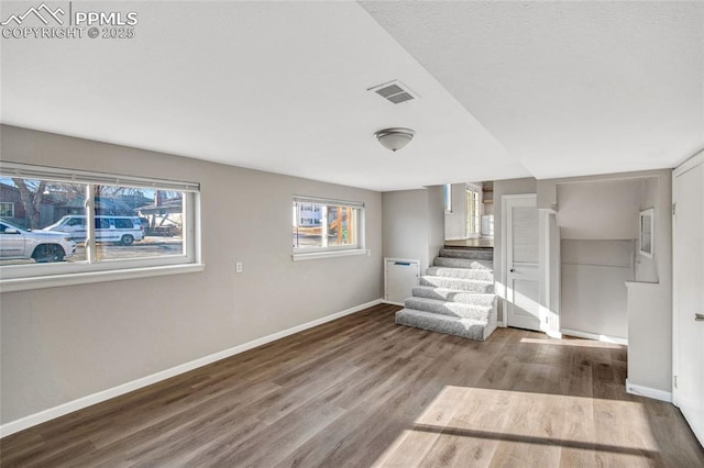 unfurnished living room with visible vents, baseboards, wood finished floors, and stairs