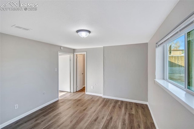 spare room featuring visible vents, baseboards, and wood finished floors