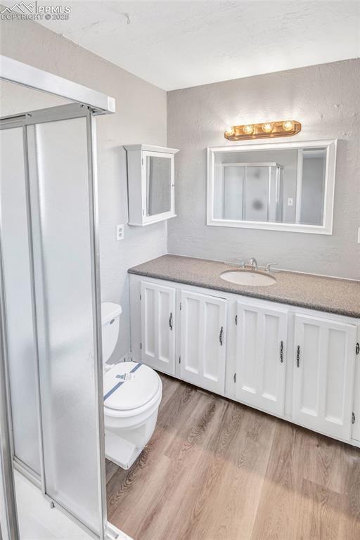 full bath featuring toilet, a stall shower, vanity, and wood finished floors