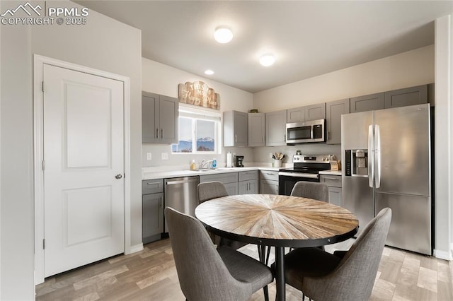 kitchen with gray cabinetry, light wood-type flooring, light countertops, appliances with stainless steel finishes, and a sink