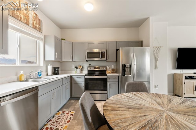 kitchen with a sink, stainless steel appliances, gray cabinetry, and light countertops