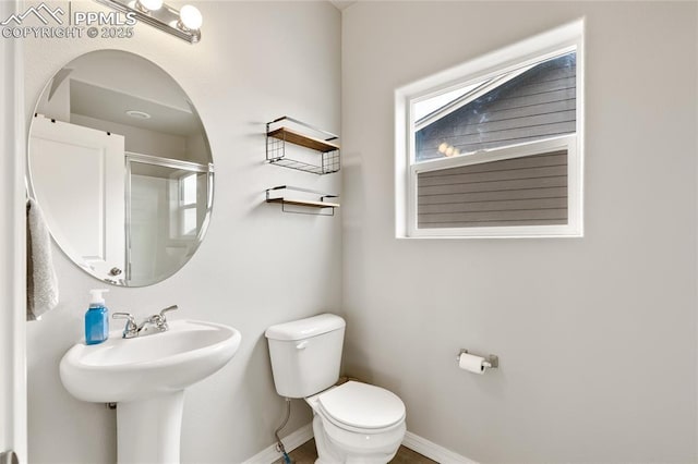 bathroom with a shower with shower door, baseboards, and toilet