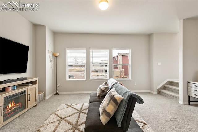 living room featuring a glass covered fireplace, stairs, light colored carpet, and baseboards