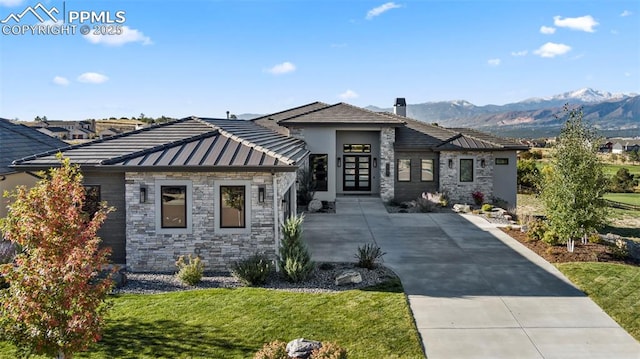 prairie-style house featuring a front lawn, metal roof, stone siding, a mountain view, and a standing seam roof