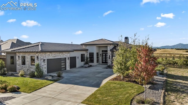 view of front of property featuring driveway, a front lawn, stone siding, an attached garage, and metal roof