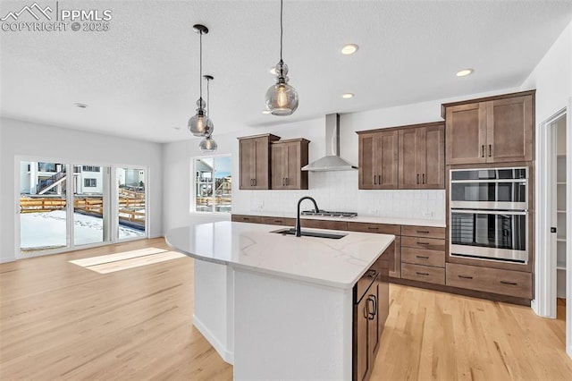 kitchen featuring double oven, wall chimney exhaust hood, light wood-style floors, and tasteful backsplash