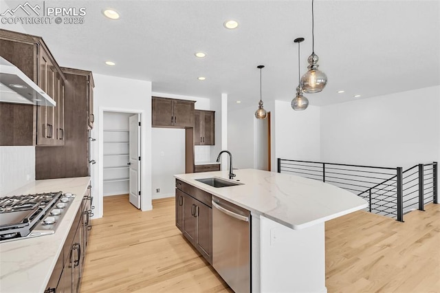 kitchen featuring light stone countertops, a sink, stainless steel appliances, dark brown cabinetry, and light wood-type flooring