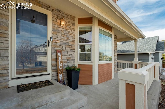 doorway to property featuring stone siding, a porch, and a shingled roof