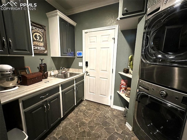 clothes washing area with baseboards, ornamental molding, stacked washer and dryer, cabinet space, and a sink