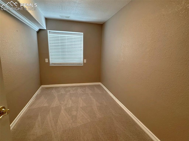 carpeted empty room featuring visible vents, a textured wall, baseboards, and a textured ceiling