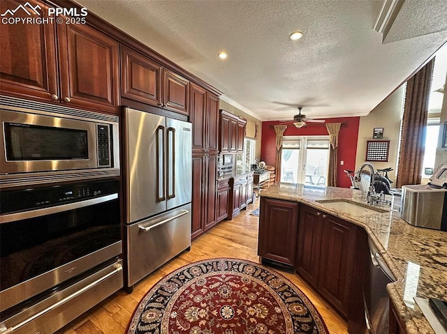 kitchen featuring a sink, light stone counters, light wood-type flooring, and stainless steel appliances