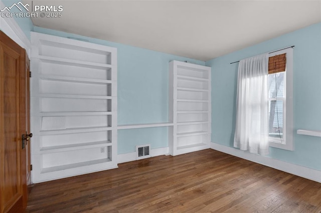 unfurnished room featuring built in features, visible vents, baseboards, and wood finished floors