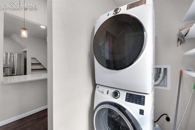 washroom featuring laundry area, wood finished floors, stacked washer / drying machine, and baseboards