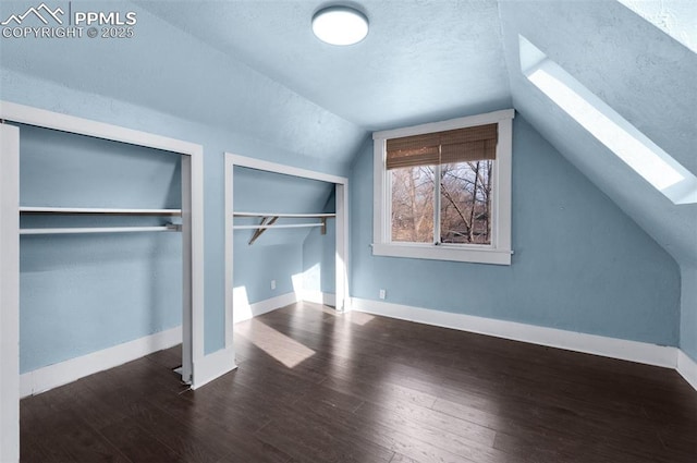 unfurnished bedroom featuring baseboards, multiple closets, wood finished floors, and lofted ceiling with skylight