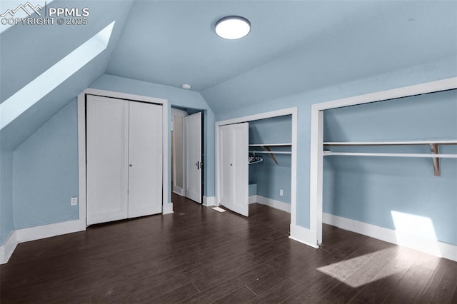 unfurnished bedroom featuring baseboards, two closets, wood finished floors, and vaulted ceiling