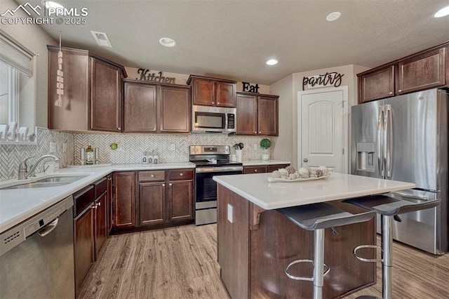 kitchen featuring a kitchen island, a sink, stainless steel appliances, dark brown cabinetry, and light wood-style floors