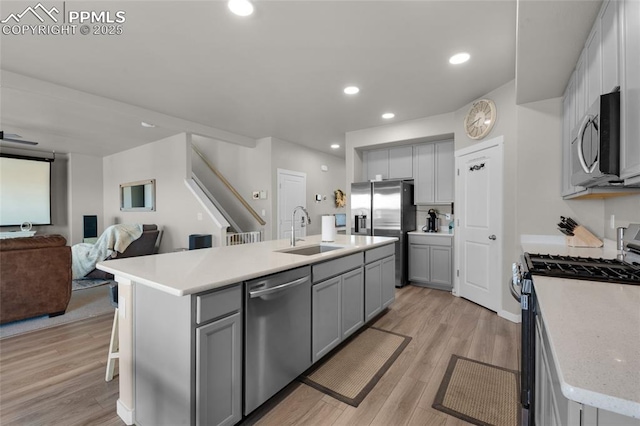 kitchen with light countertops, gray cabinets, appliances with stainless steel finishes, light wood-style flooring, and a sink