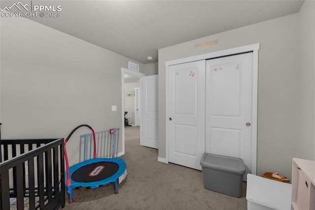 carpeted bedroom featuring a crib, visible vents, and a closet