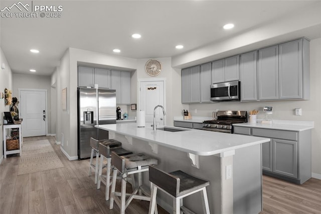 kitchen featuring light wood-type flooring, a breakfast bar, gray cabinetry, a sink, and appliances with stainless steel finishes