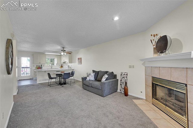 living room featuring a tiled fireplace, light colored carpet, a textured ceiling, and baseboards