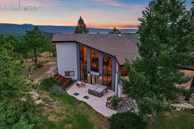 back of house at dusk with a yard, stucco siding, entry steps, a patio area, and a mountain view