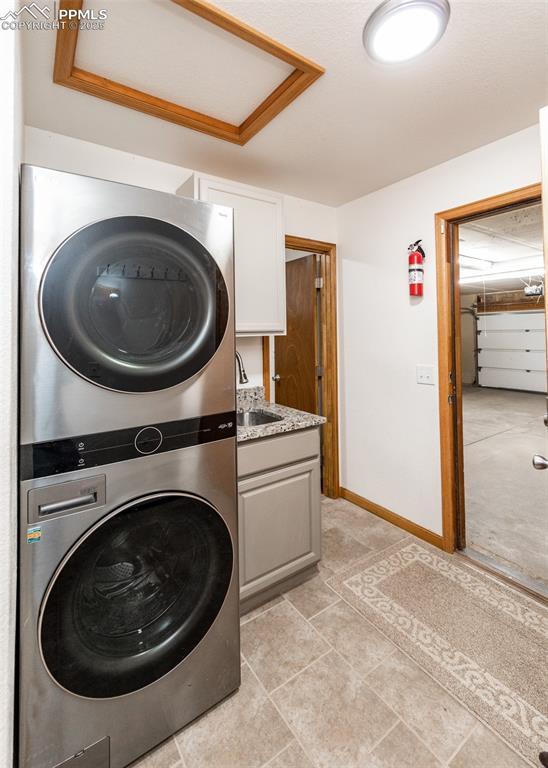 laundry room featuring cabinet space, stacked washing maching and dryer, baseboards, and a sink