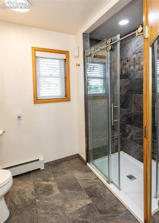 bathroom with baseboard heating, a healthy amount of sunlight, a stall shower, and toilet