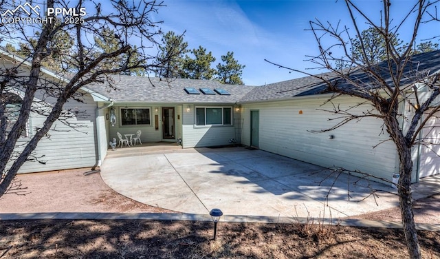 rear view of house with a patio area, driveway, and a shingled roof