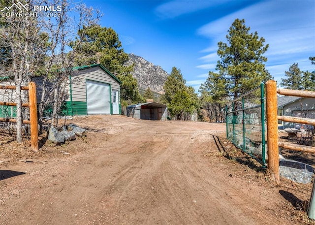 view of yard featuring an outbuilding, dirt driveway, fence, a mountain view, and a garage