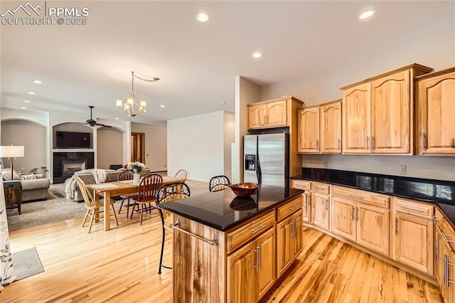 kitchen with dark countertops, a tiled fireplace, a breakfast bar, and stainless steel refrigerator with ice dispenser