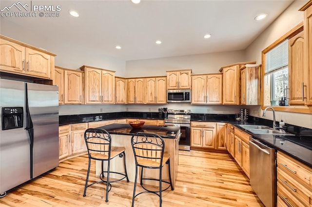 kitchen featuring a breakfast bar area, a sink, light brown cabinetry, appliances with stainless steel finishes, and a center island