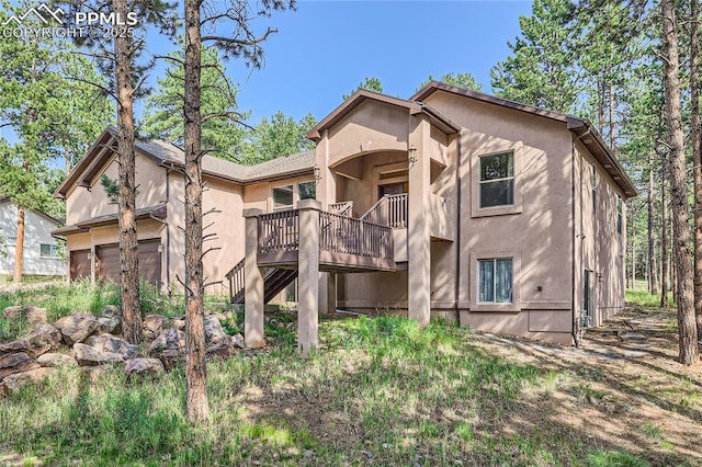 rear view of house featuring stucco siding, an attached garage, and a balcony