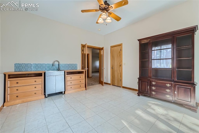 kitchen featuring light tile patterned flooring, a ceiling fan, baseboards, and a sink