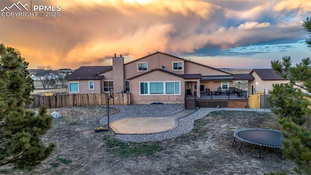 14650 Eastonville Rd, Elbert, CO 80106 - back of house featuring a wooden deck, a fenced backyard, stucco siding, a chimney, and a trampoline