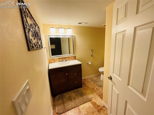 bathroom featuring visible vents, toilet, stone finish flooring, baseboards, and vanity