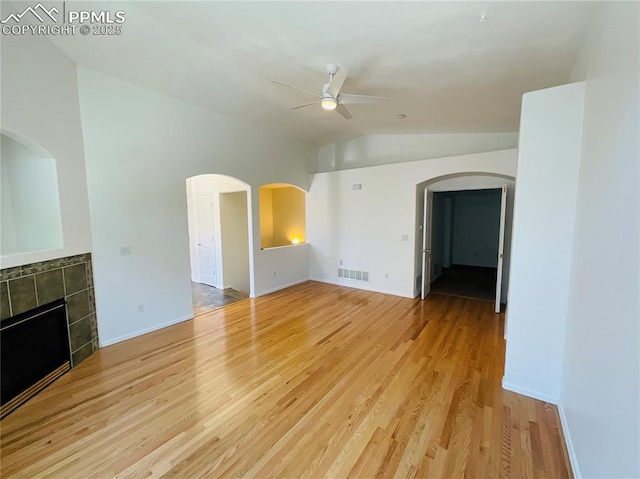 unfurnished living room with visible vents, lofted ceiling, ceiling fan, a tile fireplace, and light wood-type flooring