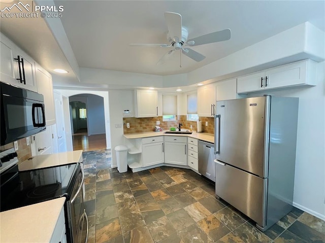 kitchen with light countertops, decorative backsplash, stainless steel appliances, arched walkways, and white cabinetry