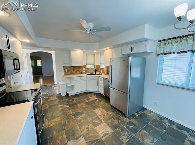 kitchen featuring arched walkways, a sink, decorative backsplash, light countertops, and stainless steel appliances